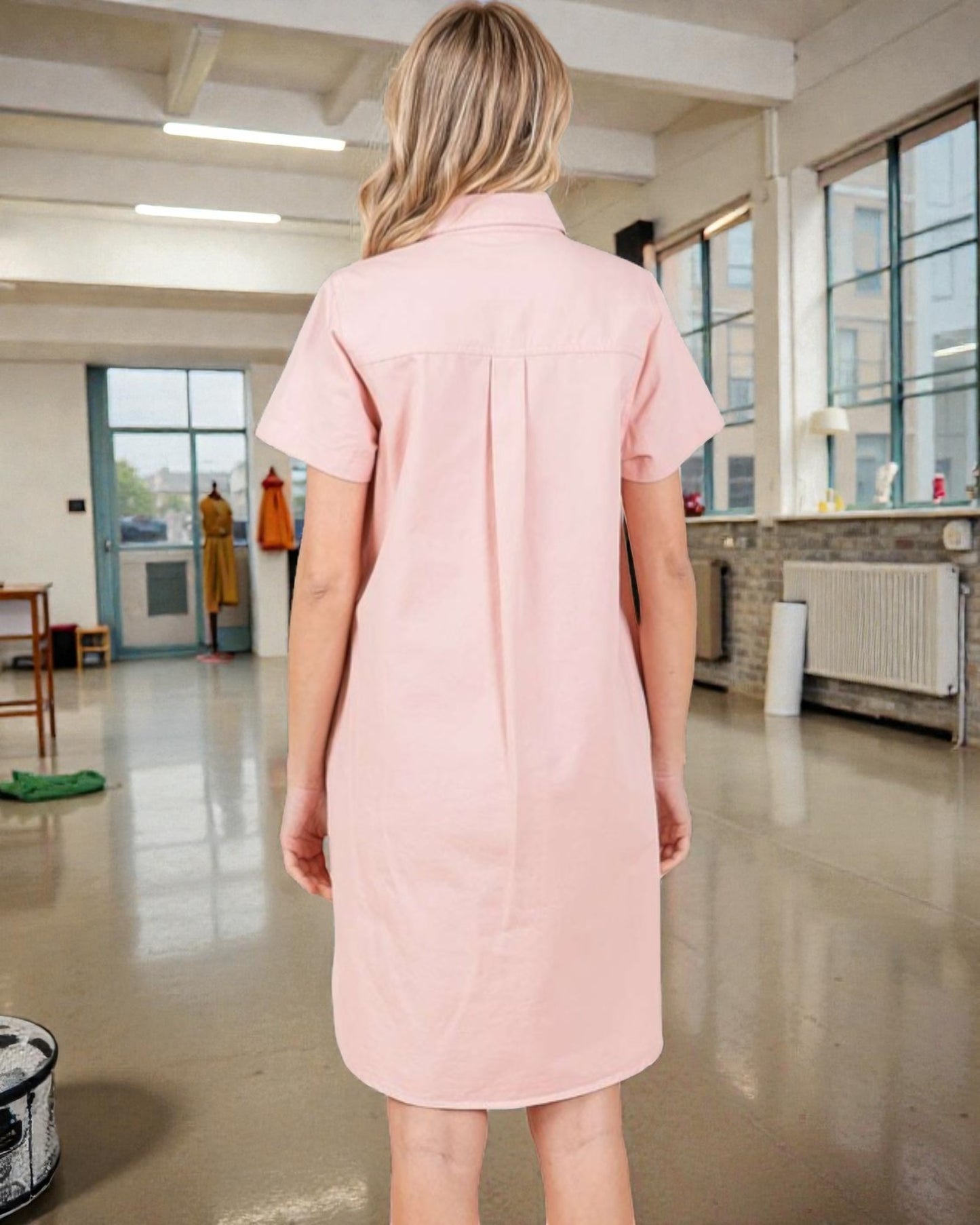 Person wearing a pink dress in an indoor setting with large windows.