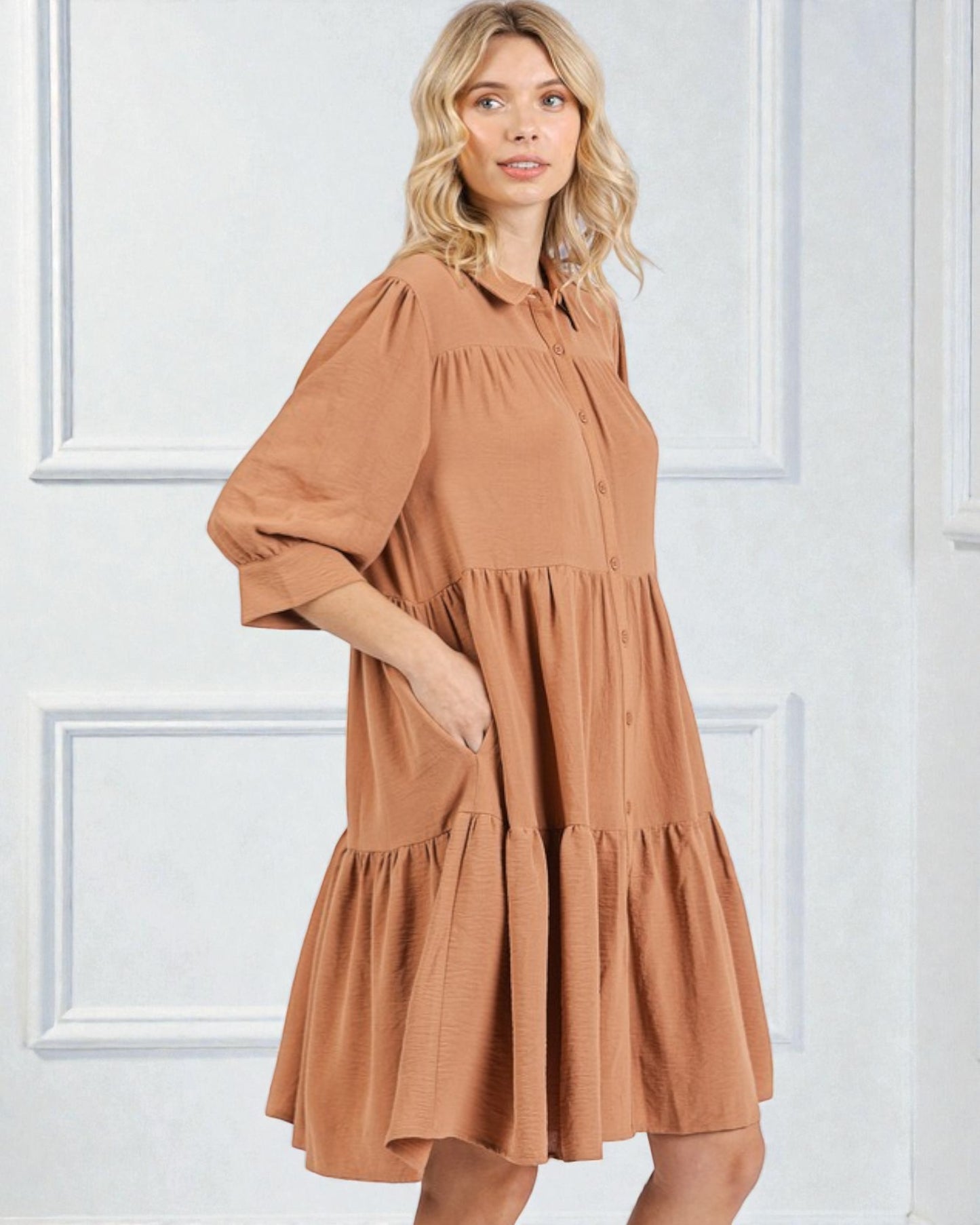 Woman wearing a brown dress against a white paneled wall