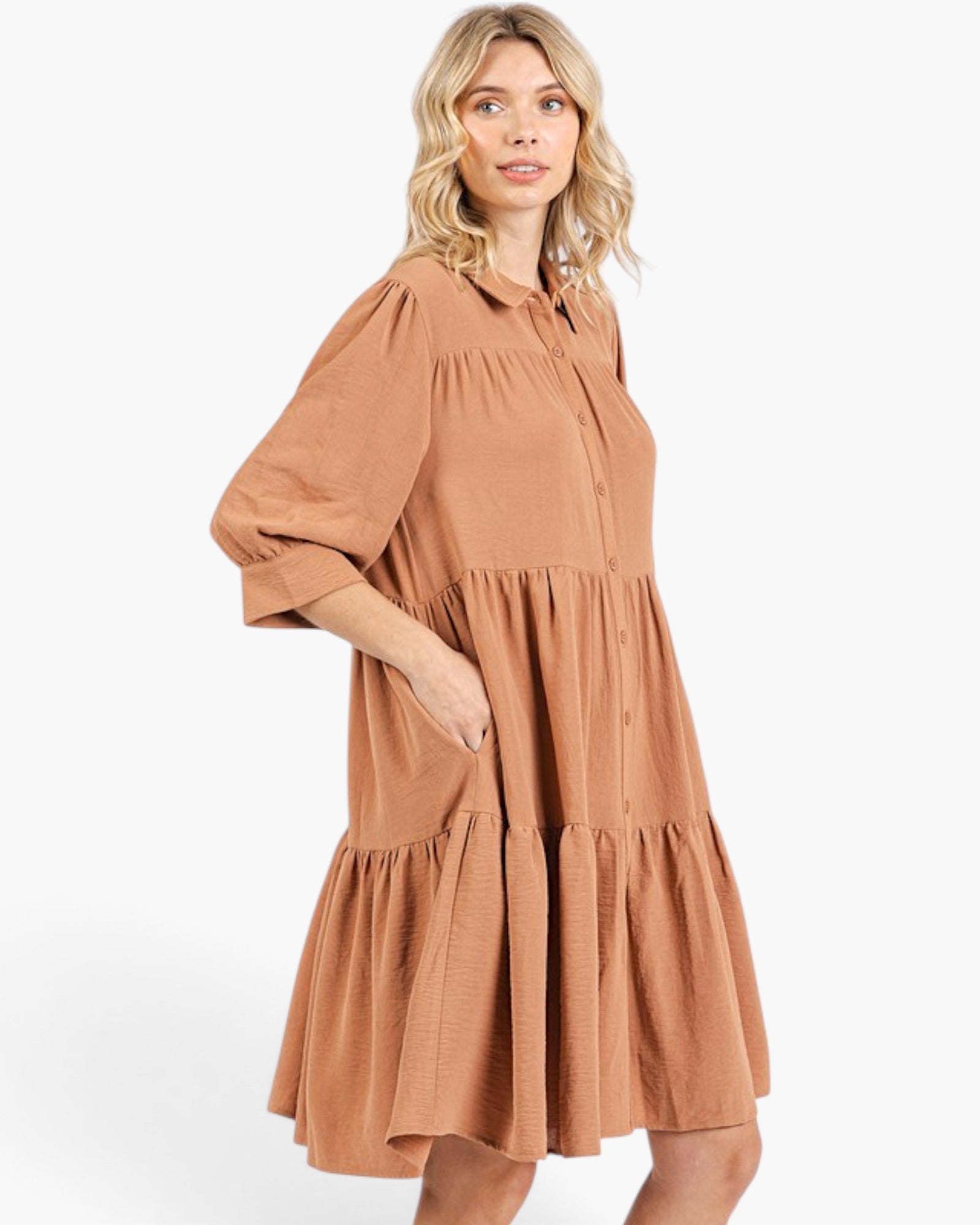 A woman wearing a tiered, short-sleeved midi dress in a warm terracotta or rust color, photographed against a clean white studio background.