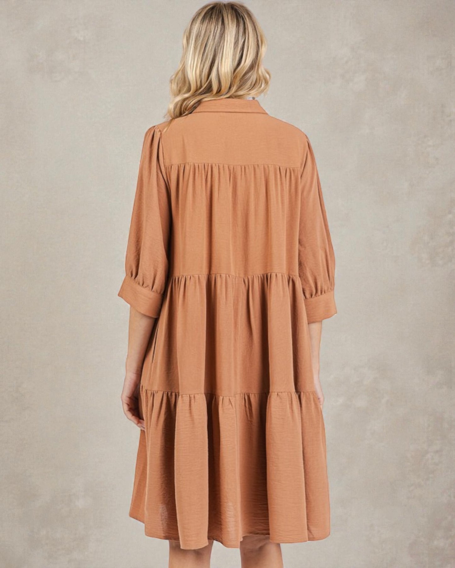 Woman wearing a brown tiered dress against a plain background