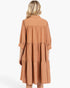 A woman viewed from the back wearing a tiered, three-quarter sleeve dress in a warm terracotta or rust color, set against a plain white studio background.