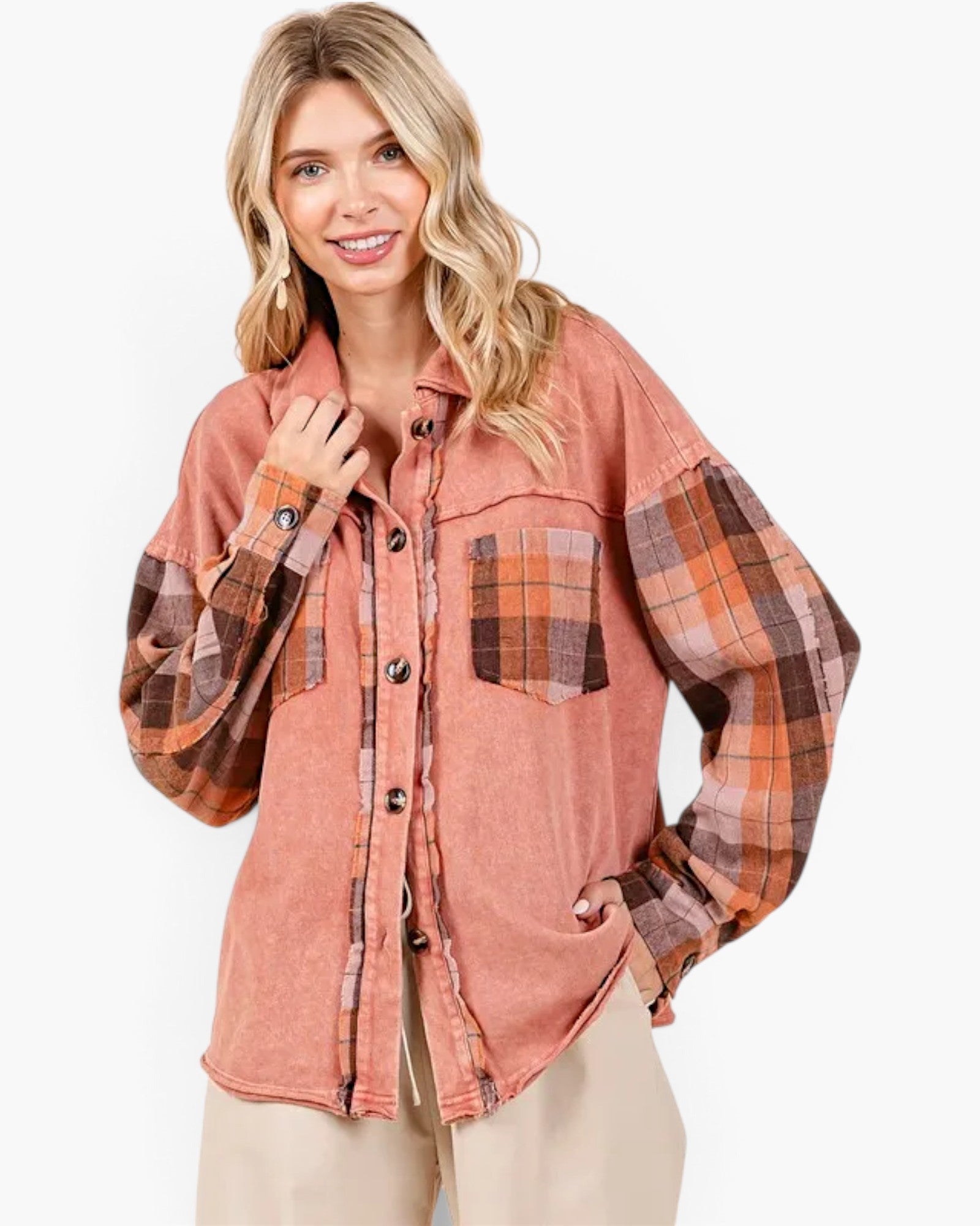 A woman wearing a rust-colored mineral-wash button-up shirt with plaid sleeves and chest pocket, paired with beige pants, against a plain white background.