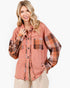 A woman wearing a rust-colored mineral-wash button-up shirt with plaid sleeves and chest pocket, paired with beige pants, against a plain white background.