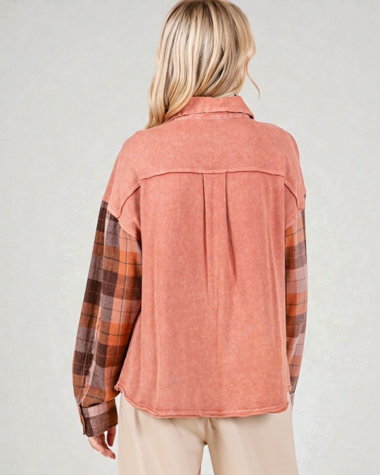 Person wearing a pink corduroy shirt over a plaid shirt with beige pants on a light gray background