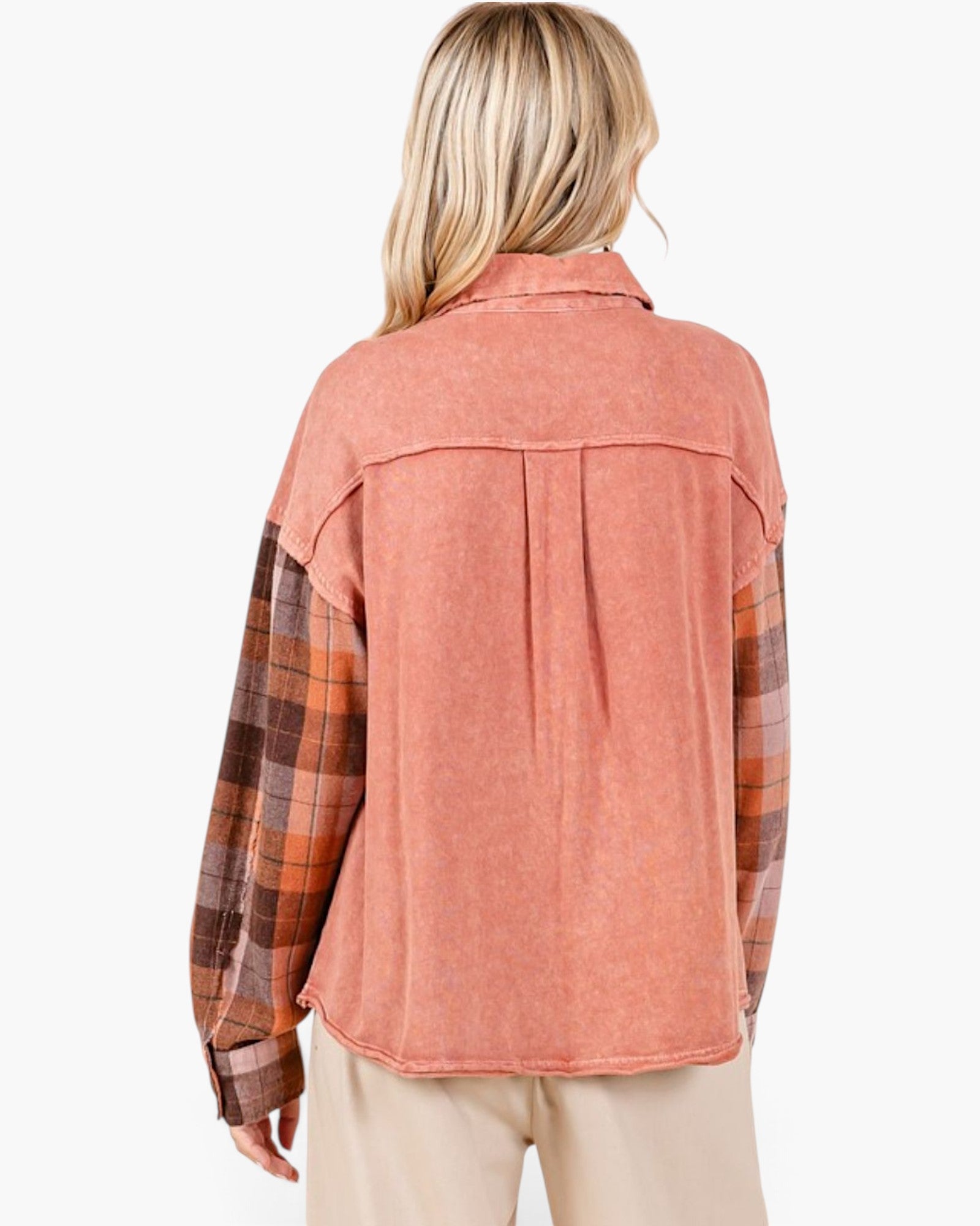 A woman shown from the back wearing a long-sleeve collared shirt with a washed coral-pink body and plaid sleeves in brown, orange, and beige tones, paired with light beige pants against a plain white background.