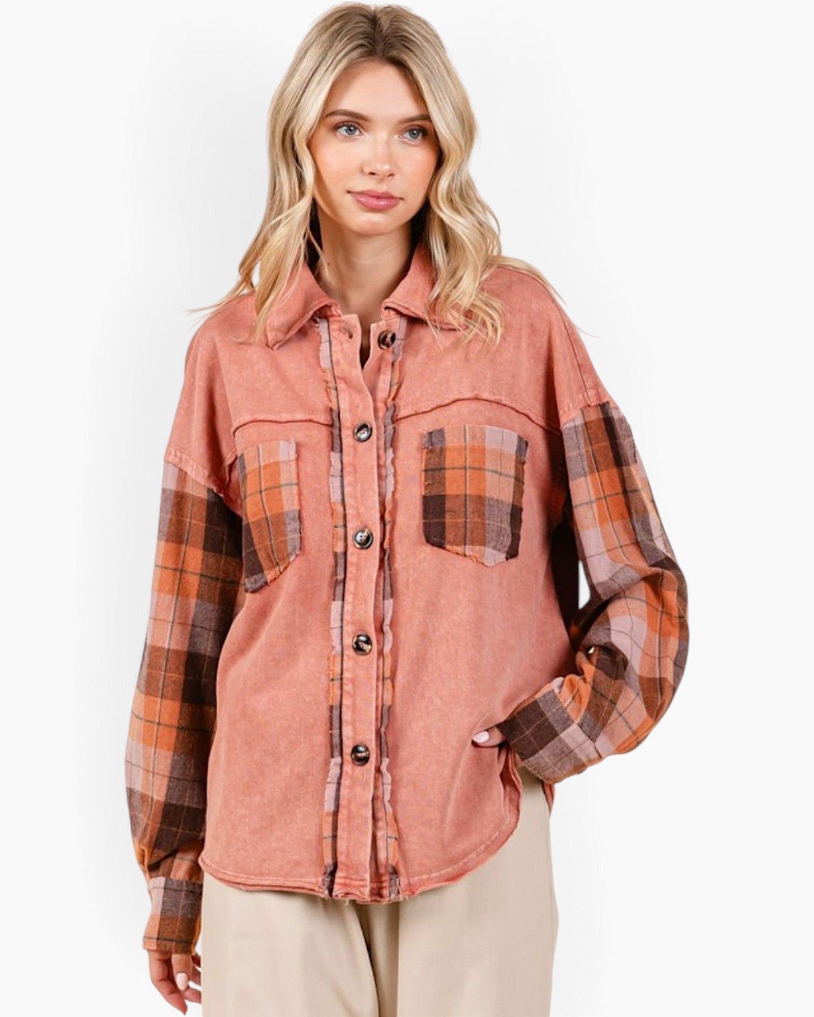 A woman wearing a long-sleeve button-up shirt with a washed terracotta body and brown plaid sleeves, paired with beige pants, against a plain white studio background.