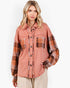 A woman wearing a long-sleeve button-up shirt with a washed terracotta body and brown plaid sleeves, paired with beige pants, against a plain white studio background.