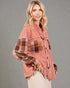 Woman wearing a plaid shirt over a pink jacket against a gray background