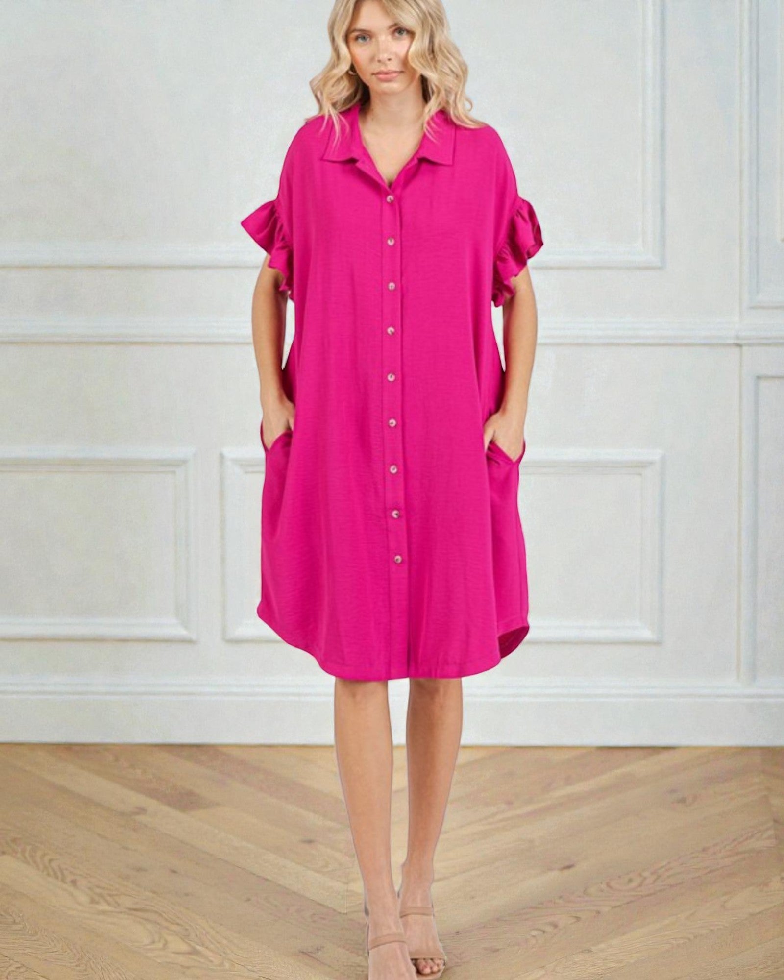 Woman wearing a bright pink dress with ruffled sleeves against a white wall.