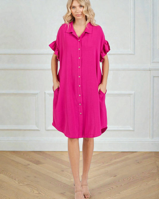 Woman wearing a bright pink dress with ruffled sleeves against a white wall.