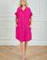 Woman wearing a bright pink dress with ruffled sleeves against a white wall.