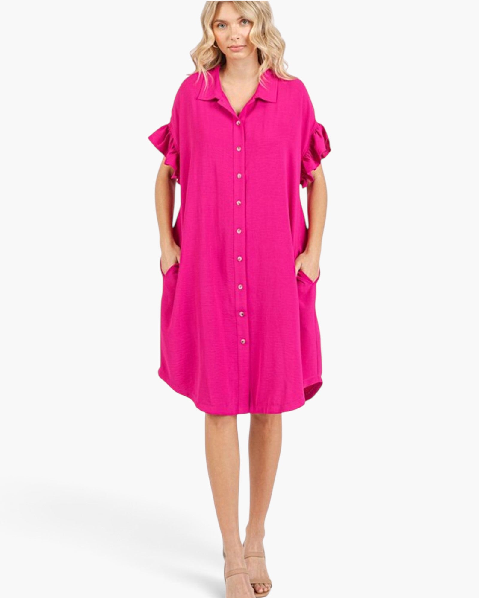 A woman modeling a bright pink button-front shirt dress with ruffled short sleeves and side pockets, photographed against a clean light gray studio background.