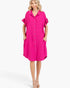 A woman modeling a bright pink button-front shirt dress with ruffled short sleeves and side pockets, photographed against a clean light gray studio background.