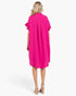 A woman viewed from the back wearing a bright pink short-sleeve midi dress with ruffled sleeves and a relaxed silhouette, paired with beige high-heeled sandals against a plain white studio background.