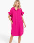 A woman modeling a bright pink short-sleeve button-up shirt dress with ruffled sleeves and side pockets, photographed against a clean white studio background.