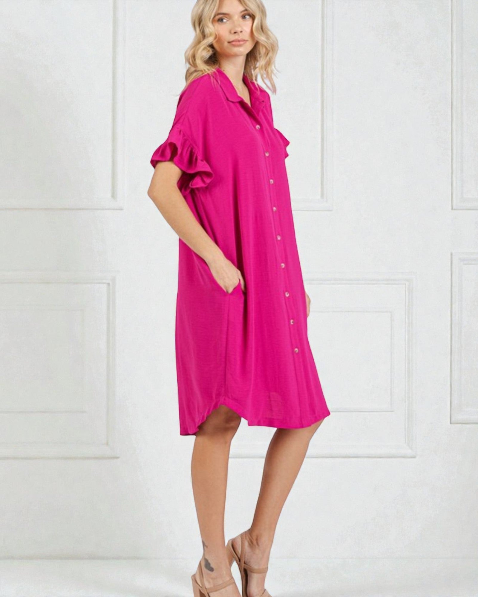 Woman wearing a bright pink dress with ruffled sleeves against a white background