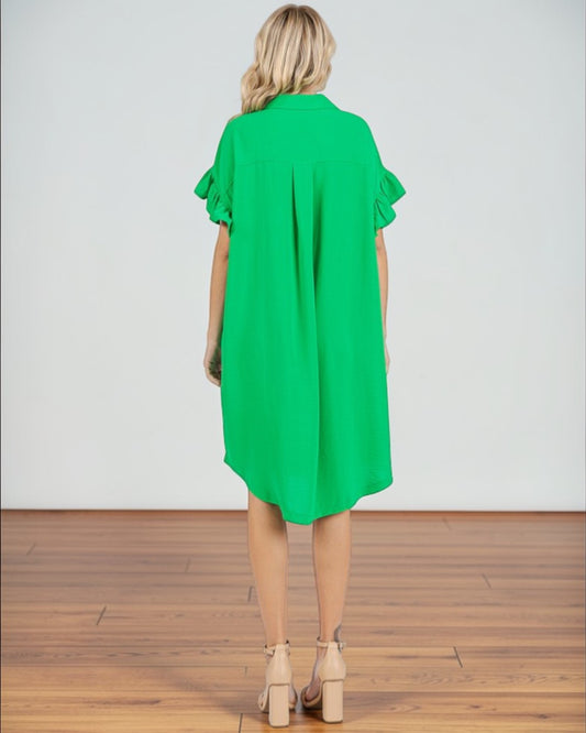 Woman wearing a green dress with ruffled sleeves on a wooden floor.
