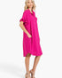 A woman modeling a bright fuchsia pink short-sleeve button-up shirt dress with ruffled sleeves and side pockets, paired with beige high-heeled sandals against a clean white studio background.