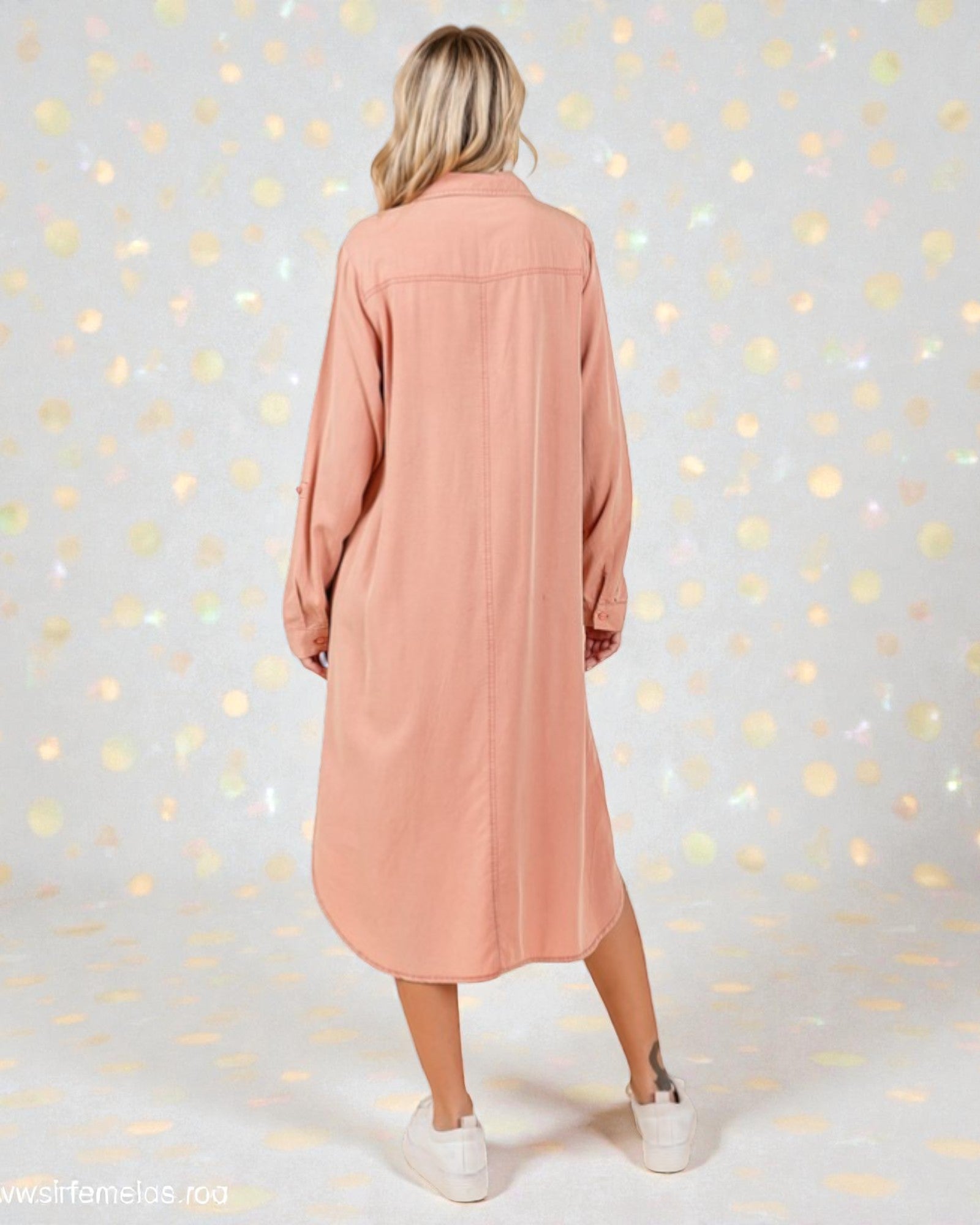 Woman wearing a long pink dress against a light gray background with gold dots.