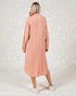 Woman wearing a long pink dress against a light gray background with gold dots.