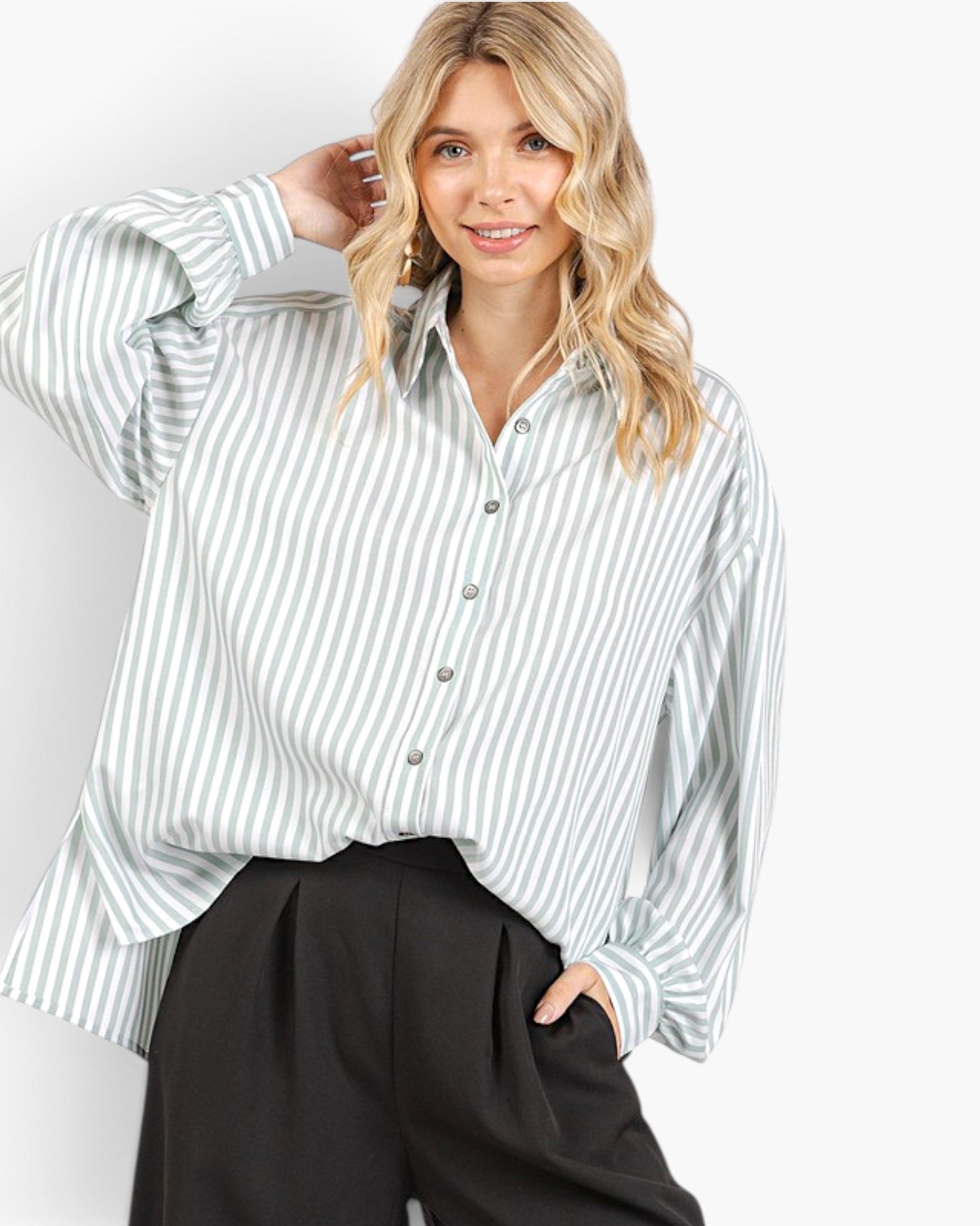 A woman wearing a light green and white vertically striped button-up shirt with black pants, posing against a light gray studio background.