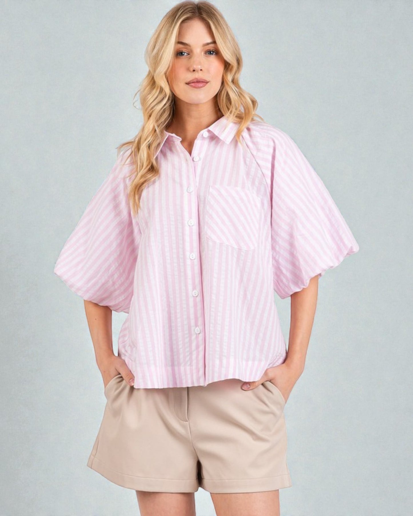 Woman wearing a light pink striped shirt and beige shorts on a gray background