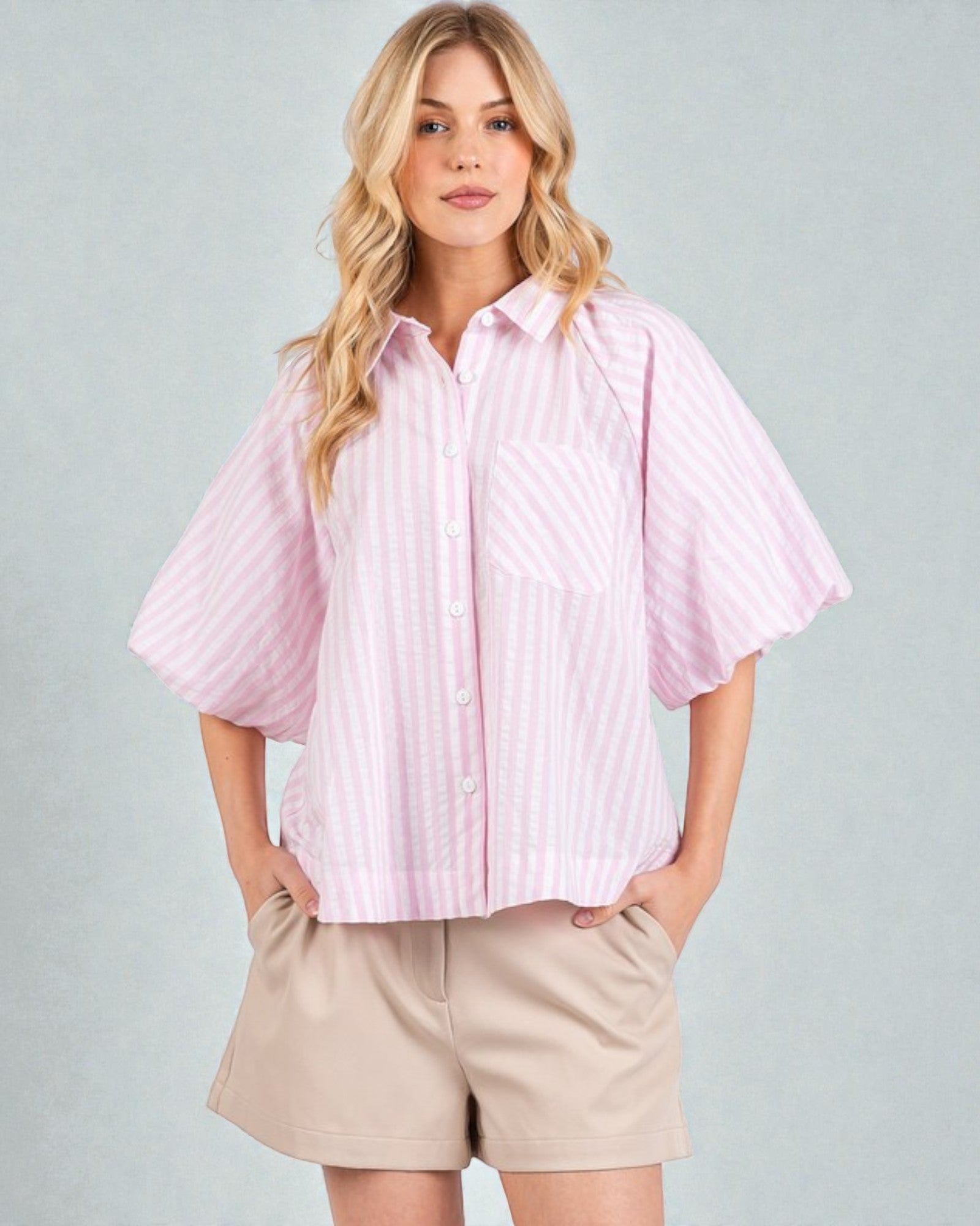 Woman wearing a light pink striped shirt and beige shorts on a gray background