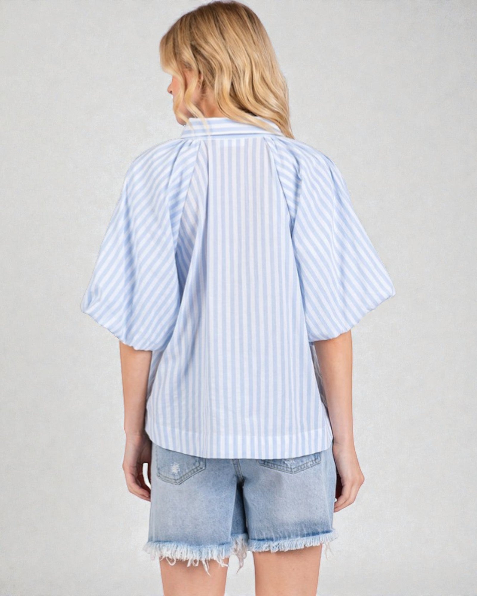 Person wearing a light blue and white striped shirt with denim shorts on a plain background