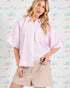 Woman wearing a pink striped shirt and beige shorts against a colorful background