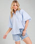 Woman wearing a light blue and white striped shirt and denim shorts on a gray background