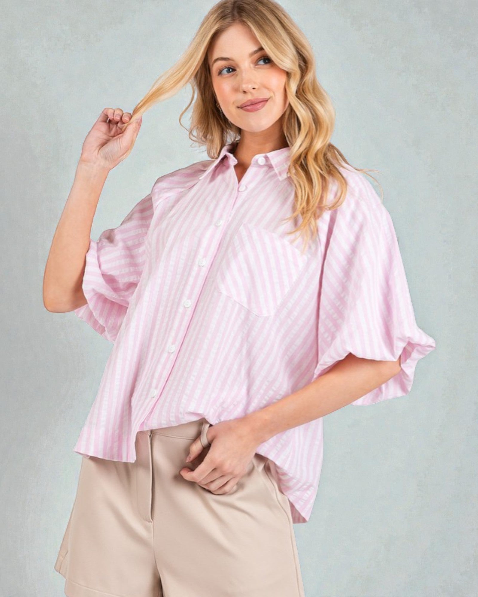 Woman wearing a pink striped shirt and beige pants against a light gray background