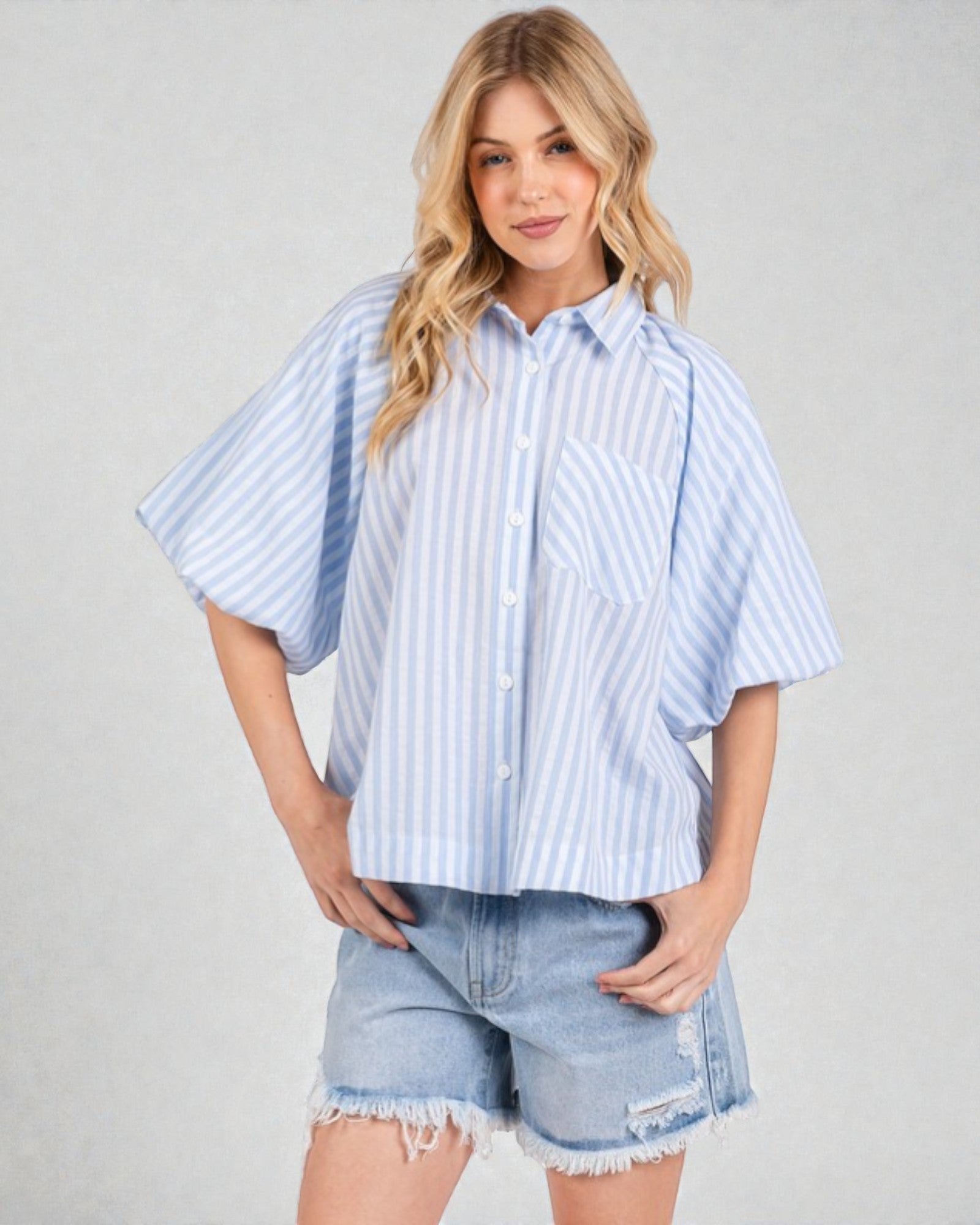 Woman wearing a light blue striped shirt and denim shorts on a plain background