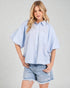 Woman wearing a light blue striped shirt and denim shorts on a plain background