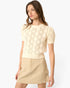 A woman modeling a cream short-sleeve knit sweater with a textured geometric pattern, paired with a beige mini skirt, against a plain white studio background.