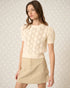 Woman wearing a cream knitted top and beige skirt against a light background