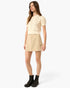 A woman modeling a cream short-sleeve knit top and beige mini skirt set, paired with black lace-up boots, against a plain light gray studio background.