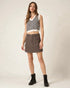 Woman wearing a patterned top and brown skirt with black boots on a plain background