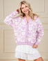 Woman wearing a purple cardigan with heart patterns against a beige wall.