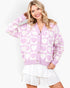 A smiling blonde woman models a pink and white knit cardigan with a heart pattern, paired with a white tiered skirt, against a clean white background.