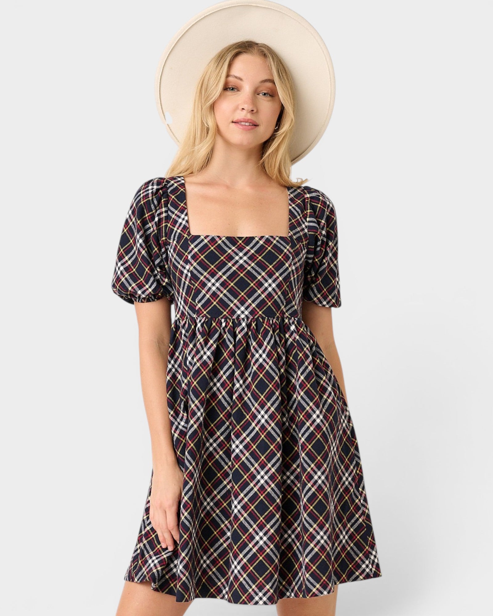 Woman wearing a plaid dress with a beige hat on a white background