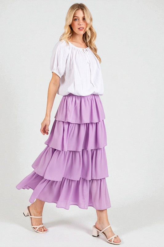 Woman wearing a white top and purple tiered skirt on a white background