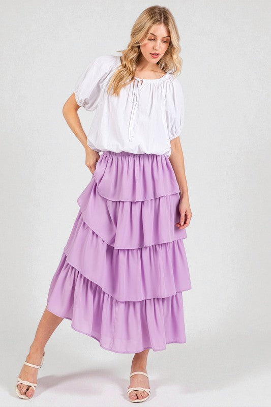 Woman wearing a white blouse and purple tiered skirt on a plain background