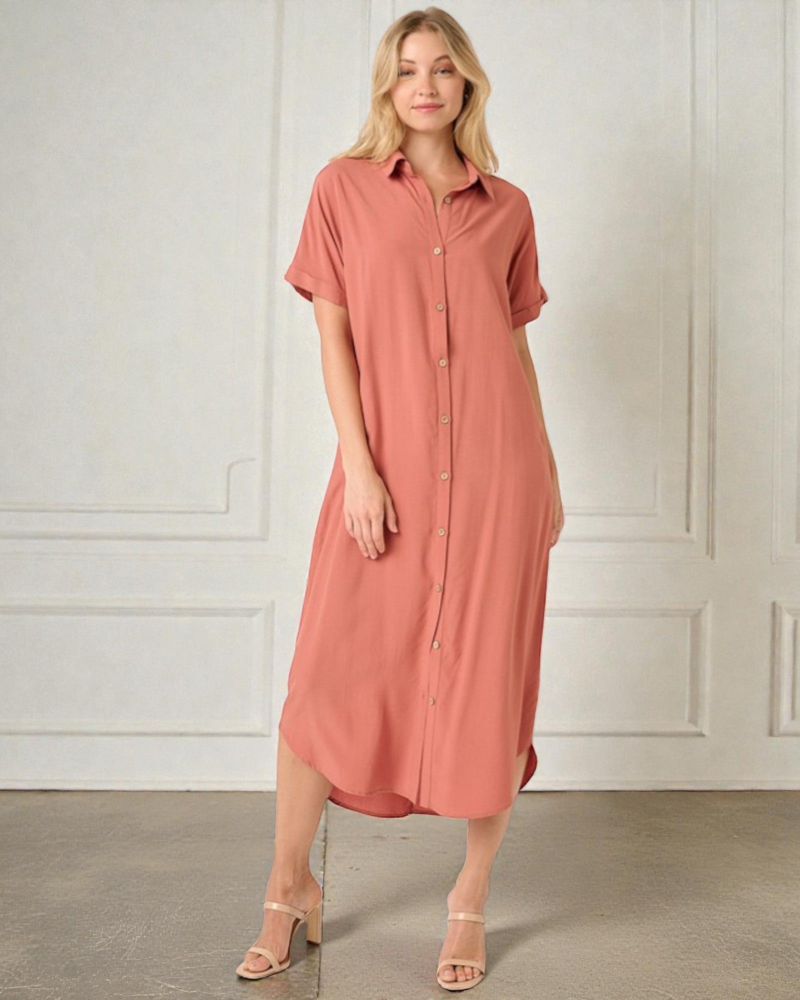 Woman wearing a pink dress standing against a white wall.