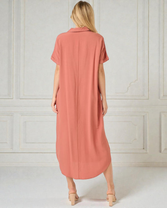 Woman wearing a long coral dress against a white paneled wall.