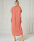 Woman wearing a long coral dress against a white paneled wall.