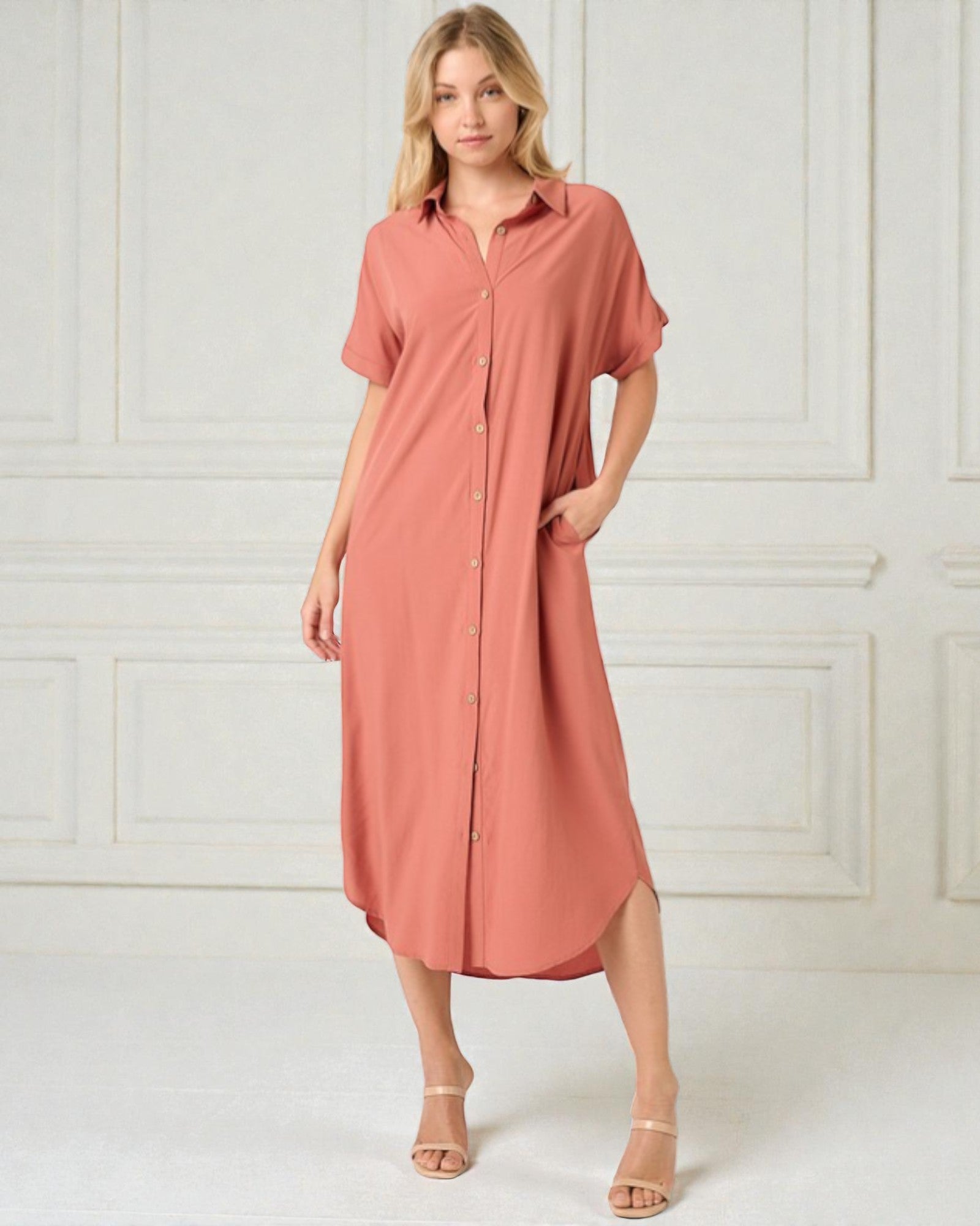 Woman wearing a pink shirt dress against a white paneled wall.