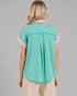 Person wearing a teal blouse with pink accents on a gray background