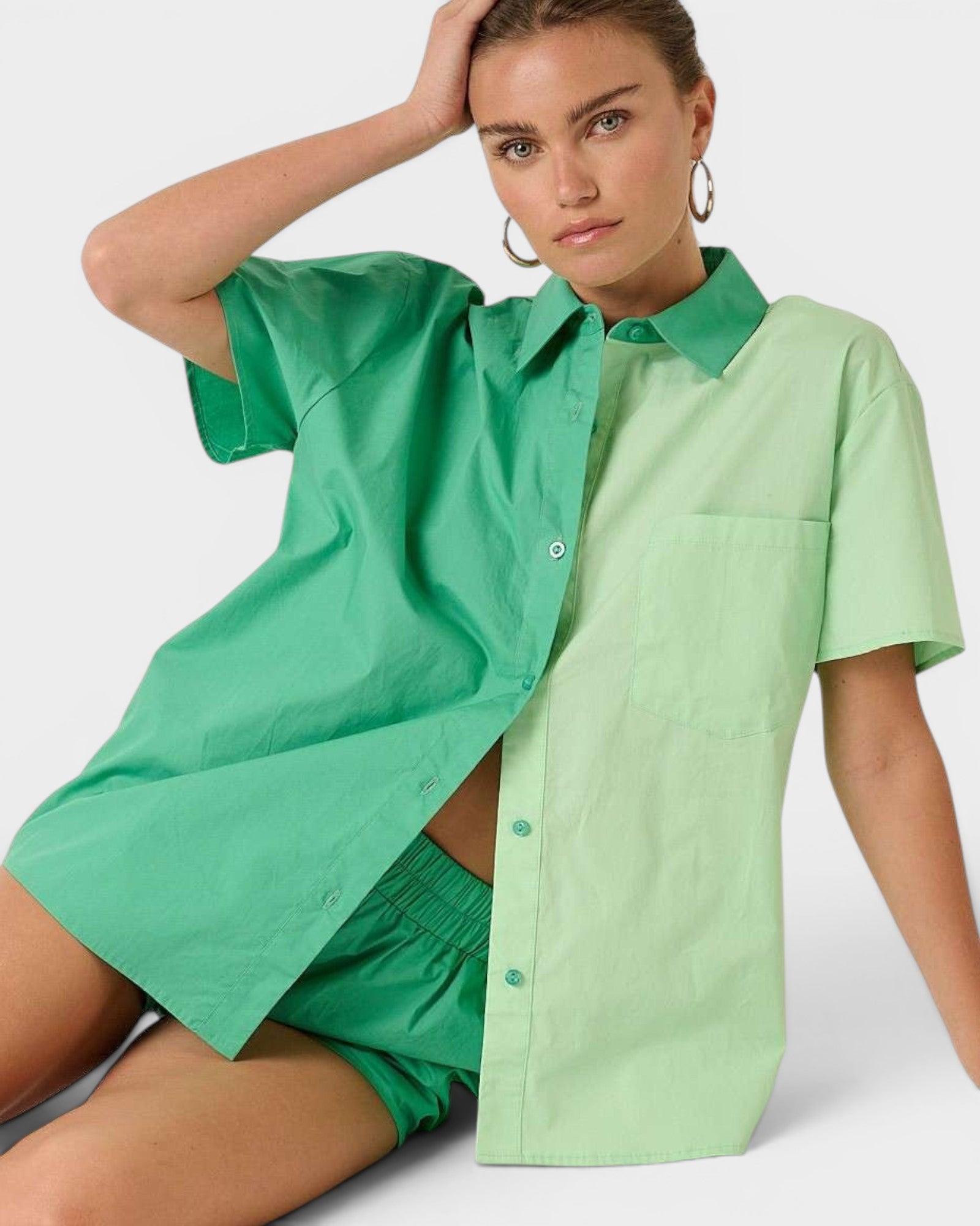 Woman wearing a green and light green button-up shirt with green shorts on a white background