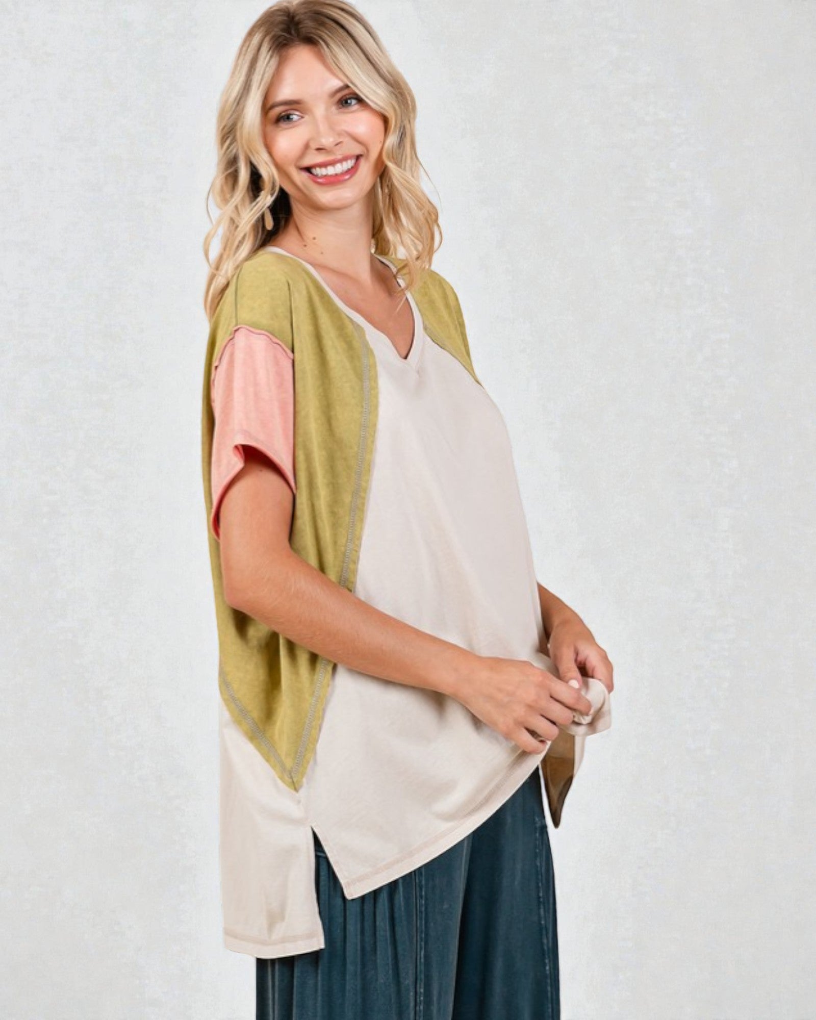 Woman wearing a green cardigan over a white top with a pink sleeve, standing against a white background.