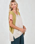 Woman wearing a green cardigan over a white top with a pink sleeve, standing against a white background.